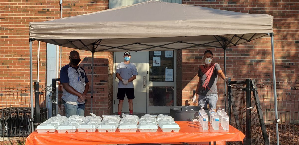 Photo of people in masks under a tent with meals and water